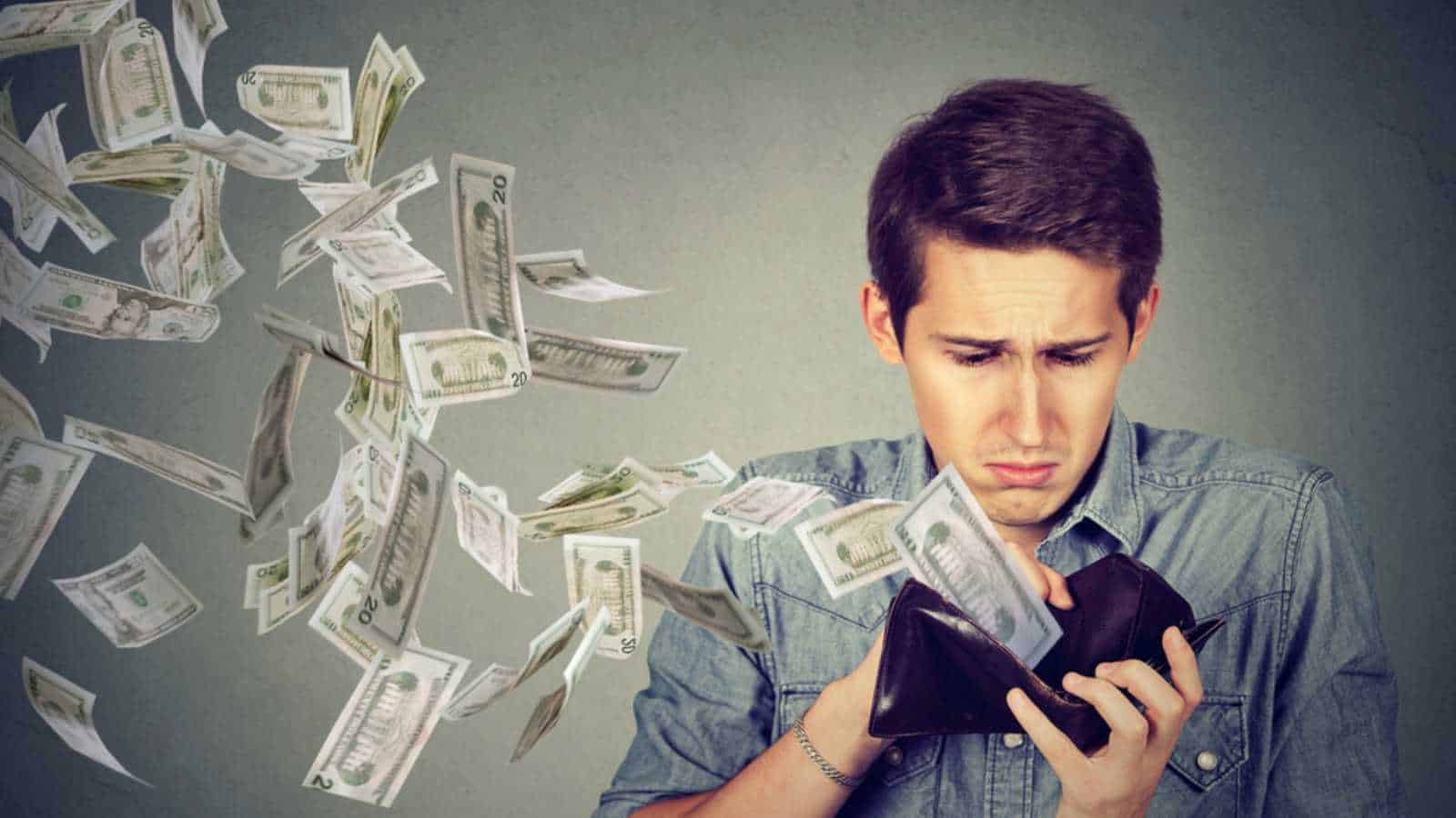 Sad man looking at his wallet with money dollar banknotes flying out away