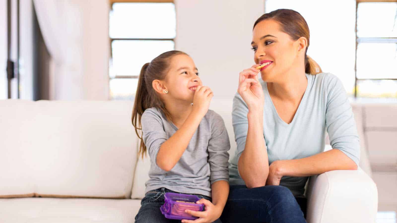 happy mother and daughter eating crackers at home