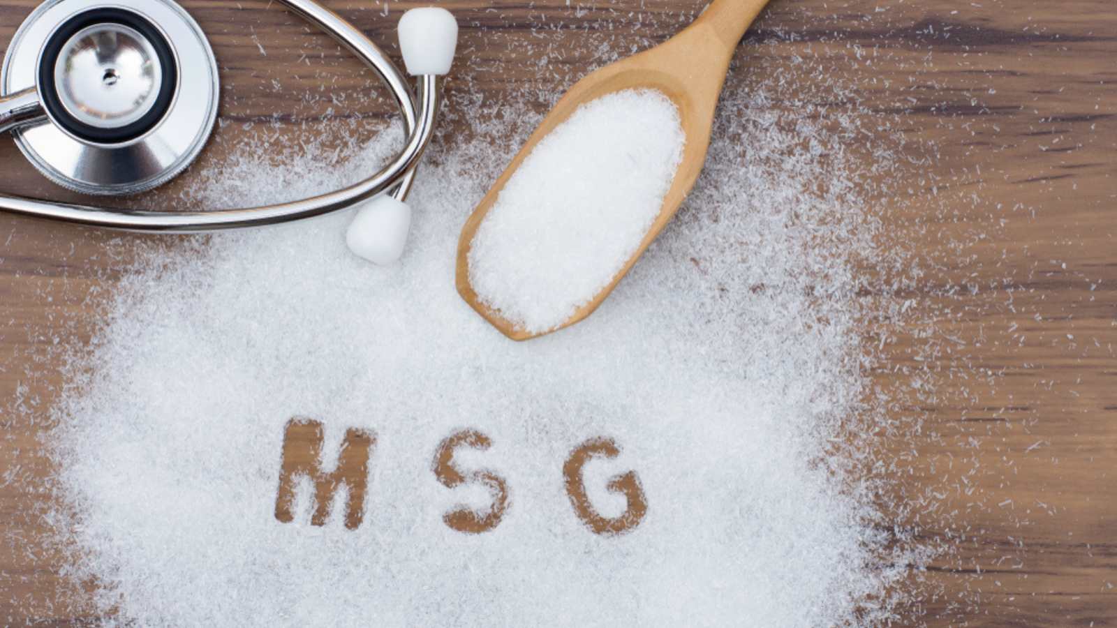 Monosodium glutamate (MSG ), ingredients in wooden spoon and words " MSG " with medical stethoscope isolated on the wood table background. Unhealthy food concept. Top view. Flat lay