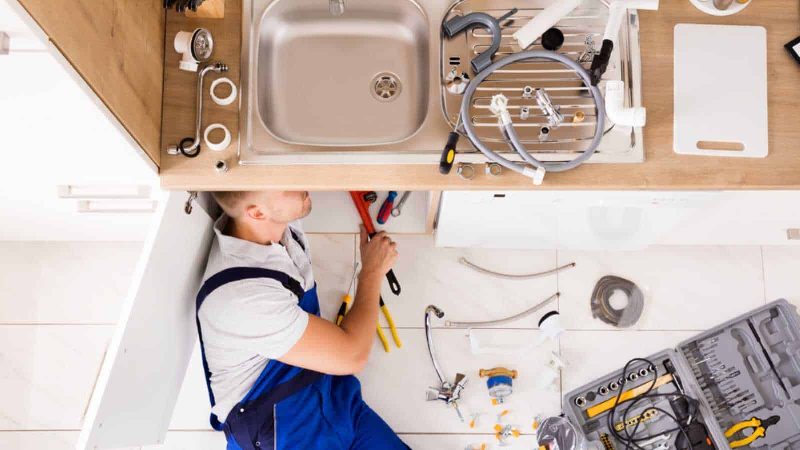 High Angle View Of Male Plumber In Overall Fixing Sink Pipe