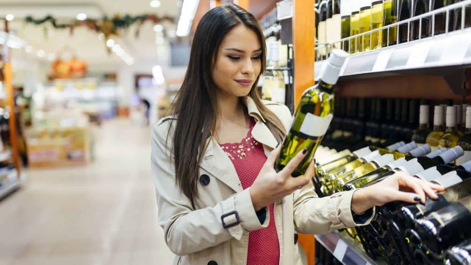 Woman deciding what wine to buy and shopping in supermarket